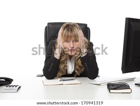 Depressed businesswoman at her wits end sitting morosely at her desk with her hands to her head staring balefully at the camera