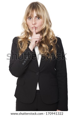 Beautiful young woman making a shushing gesture as she raises her finger to her lips asking for silence or that the viewer join her in keeping a secret, isolated on white