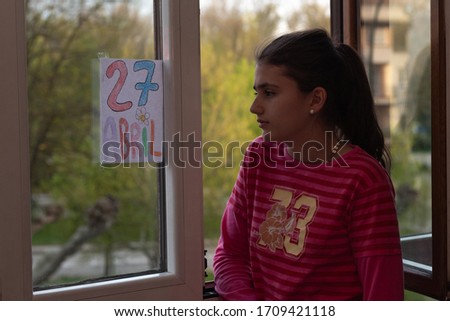 girl in pink t-shirt looking out the window wishing to go out on the street on April 27th after the confinement in the houses of Spain