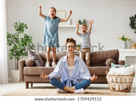 Happy mother with closed eyes meditating in lotus pose on floor trying to save inner harmony while excited children jumping on sofa and screaming in light spacious living room
 Royalty-Free Stock Photo #1709429152