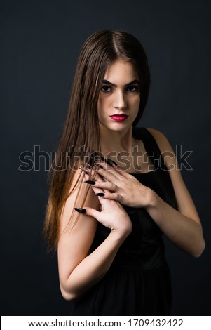 Portrait of beautiful woman in black dress with curly hair - isolated on dark background.