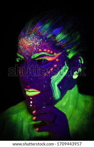 Woman in neon light, portrait of beautiful model girl with fluorescent make-up, Body Art design in UV, painted face, colorful make up, over black background
