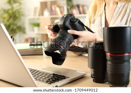 Close up of photographer woman hands with laptop checking dslr camera on a desk at home