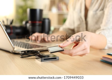 Close up of photographer woman hands plugging memory card to laptop on a desk at home