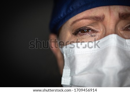Tearful Stressed Female Doctor or Nurse Wearing Medical Face Mask on Dark Background. Royalty-Free Stock Photo #1709456914