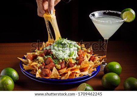 Large nachos plate with melted cheese, meat and sour cream served with a Margarita Royalty-Free Stock Photo #1709462245