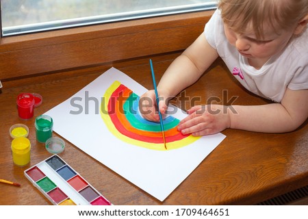Little girl drawing rainbow. Sign of hope during coronavirus outbreak. Quarantine fun. Arts and crafts for kids. Kids paint. School kid doing art homework.