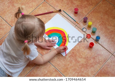 Kid painting rainbow at home during coronavirus pandemic concept. Let's all be well. Stay at home Social media campaign. Children Chase the rainbow