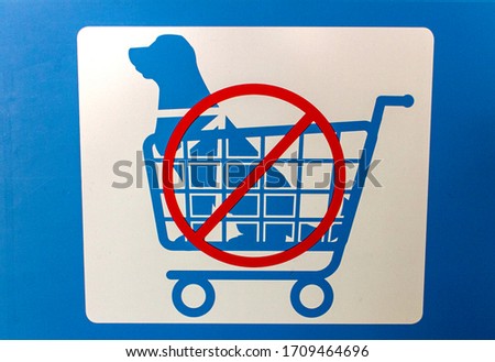 Sign in blue and white with graphic of a dog in a shopping cart indicating No Dogs Allowed In Shopping Carts with red circle backslash no symbol