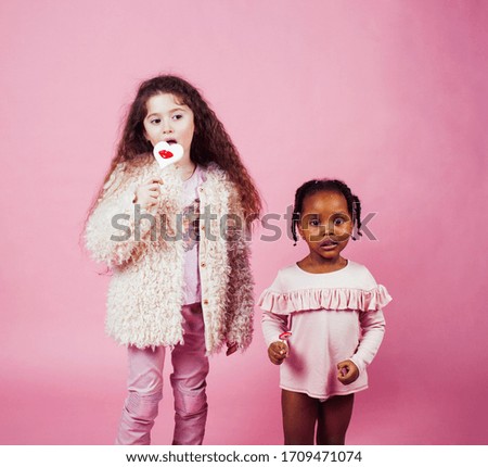lifestyle people concept: diverse nation children playing together, caucasian and african american on pink background