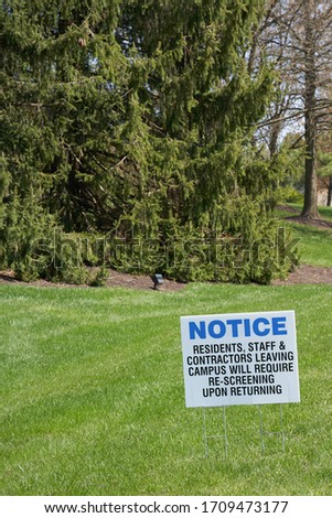 sign on a green lawn with tree behind giving notice that residents, staff and contractors leaving this senior living complex will be screened for coronavirus upon return