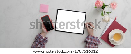 Top view of female freelancer working on  blank screen tablet and smartphone on marble desk with supplies and tea cup   