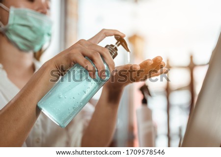 Office worker working from home during coronavirus outbreak cleaning her hands with sanitizer gel and wearing protective mask. Coronavirus, covid-19, Work from home (WFH), Social distancing concept. Royalty-Free Stock Photo #1709578546