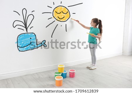 Cute child drawing sun and whale on white wall indoors