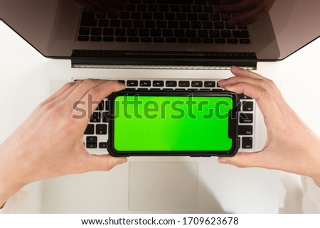 Woman with smartphone on laptop.