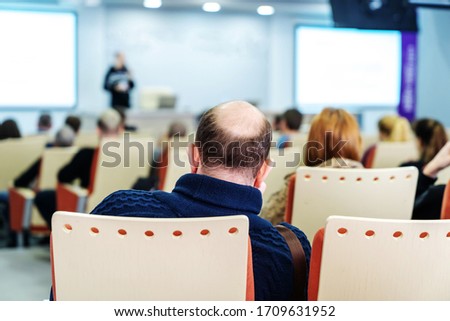 Bald man in a conference room at a lecture. Business training for continuing education. Back view. Unrecognizable faces