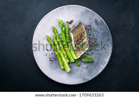 Fried gourmet skrei cod fish filet with green asparagus and lettuce offered as top view on a modern design plate with copy space 