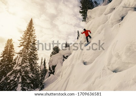 Snowboarder male jumping above snowy ski slop. Sunny day in ski resort, beautiful mountains landscape