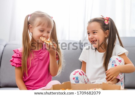 Two little girls eating huge pizza at home