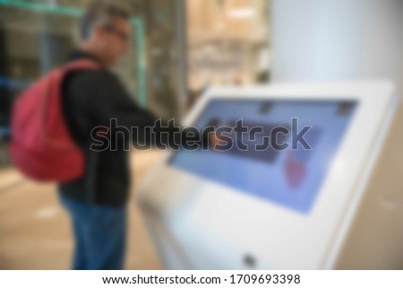 Abstract blurred man using a touch screen information point in inside a shopping mall.
