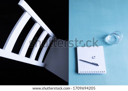 A farewell letter lies on the table next to the ring. Growing and divorce concept. White wooden chair on a black background and a blue table with a glass of water and a notebook and pen top view.