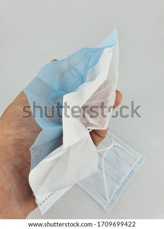 hand holding a face mask been cut into half to show its 3ply layers inside, isolated in white background.