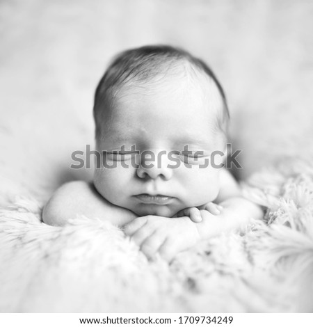 Newborn baby toddler boy or girl lies on hands on the fur and sleeps sweetly. Black and white picture