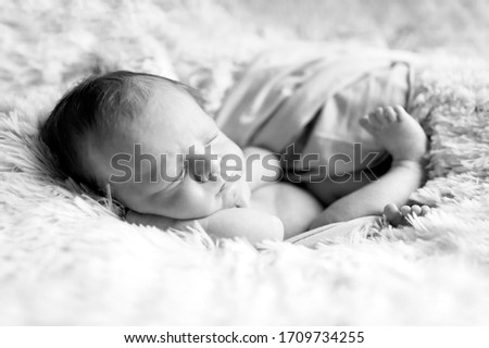 sweet and beautiful sleeping newborn baby boy or girl. Lies in the fur with wrap and sleeps. Black and white picture