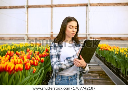 Beautiful young smiling girl with tablet in uniform, worker with flowers in greenhouse. Concept work in the greenhouse, flowers. Copy space – stock image
