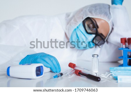 Stressed female doctor sitting tired at his desk. Mid adult female doctor working long hours in protective clothes. Covid-19 overworked doctor in his office needs a break.