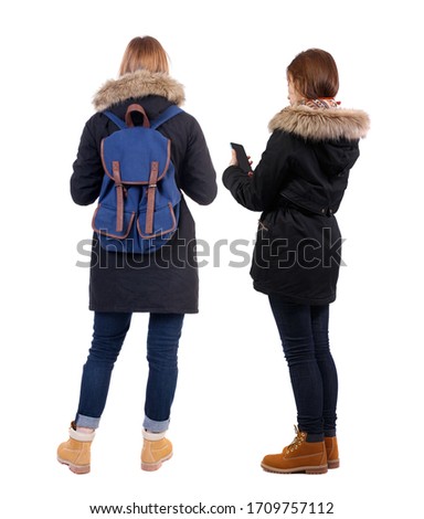 Back view of two young woman photographed on a mobile phone in winter jacket. Rear view people collection. backside view of person. Rear view. Isolated over white background.
