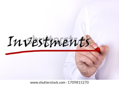 A person writes text, a word, the phrase Investments with marker on a light background. Business concept.
