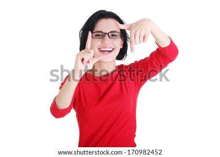 Smiling woman wearing red blouse is showing frame by hands. Happy girl with face in frame of palms. Isolated on white background. 