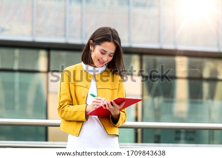 Happy beautiful Asian business woman with clipboard. Portrait Of Successful Business Woman Holding clipboard. Photo business woman wearing suit and holding documents in hands. Panoramic windows