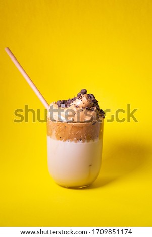 Dalgona coffee with chocolate chips isolated on yellow background. Korean trendy coffee. Vertical picture.