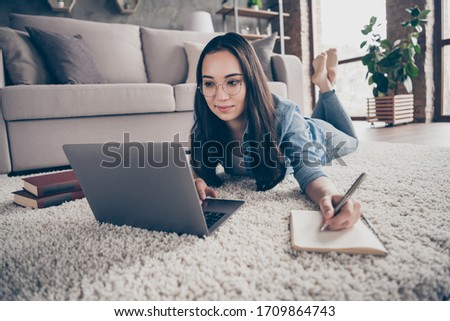 Photo of pretty asian lady lying floor carpet near couch staying home good mood quarantine time browsing notebook writing notes personal planner distance study living room indoors