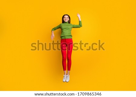 Full length photo of funny lady jumping high showing robot movement at discotheque party wear casual trendy green jumper red pants isolated yellow color background