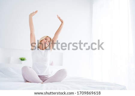Portrait of her she nice attractive lovely dreamy cheery senior woman sitting in bed stretching waking up fresh start yoga practicing in modern light white interior room flat apartment indoors Royalty-Free Stock Photo #1709869618