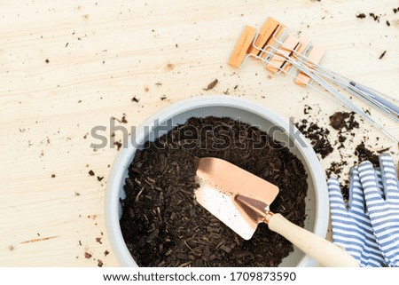 Small planting pot with topsoil and small garden shovel on a wooden table.