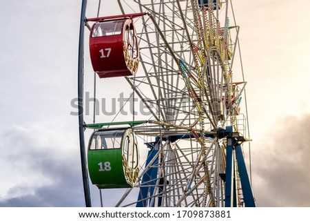Ferris wheel with multi-colored cabs against the sky with clouds and sunbeams in the park on a sunny spring day.