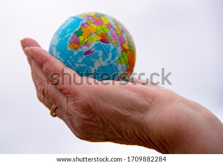 The globe on the palms of an elderly woman on a light gray background.