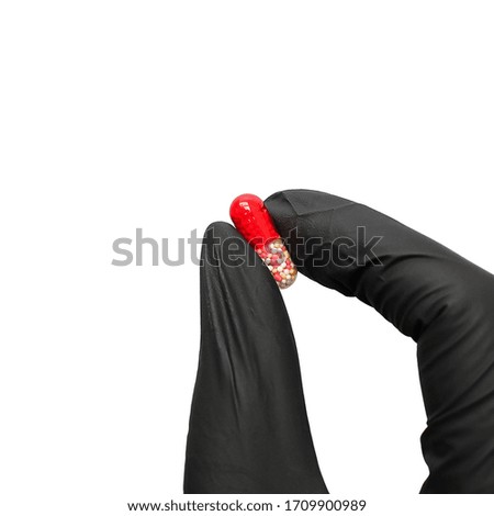 A hand in a black medical glove holds a life-saving capsule/ tablet/ pill.