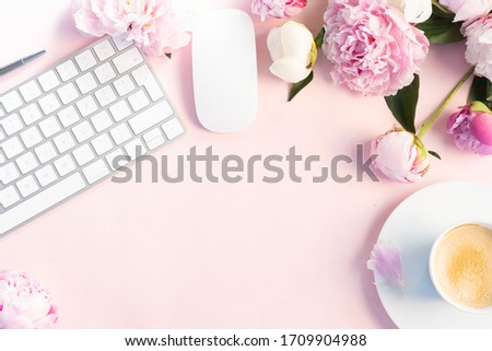 Flat lay home office workspace - modern silver keyboard with female accessories and fresh peony flowers, copy space on pink background