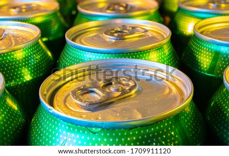 A close-up of green beer cans lit with blue and orange colored light. The cans are close together and are wet with drops of water. The cans are printed with dots.