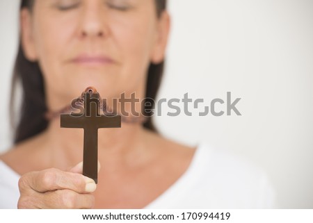 Portrait woman in blurred background holding christian symbol of crucifix in hand.