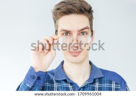 Young man in blue shirt and glasses on light grey background. Man holding glasses