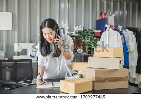 Young business woman working online e-commerce shopping at her shop. Young woman seller prepare parcel box of product for deliver to customer. Online selling, e-commerce. Royalty-Free Stock Photo #1709977465