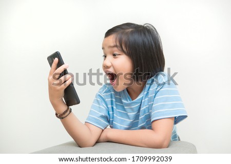 Young girl kid got shock and surprise when looking at smartphone device screen. Unsuitable content for children on internet or social media. Portrait of Asian kid on white background. Royalty-Free Stock Photo #1709992039