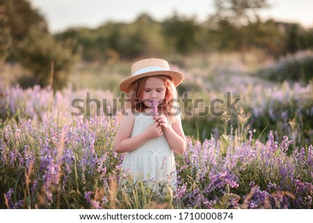 the child sniffs a flower in the field, a girl in a straw hat among the flowers. Children Protection Day
