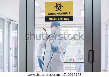 Asian man wear personal protective suits or PPE, goggles, mask, and gloves making disinfection and decontamination on quarantine room with coronavirus alert sign. Covid-19 and disinfection concept Royalty-Free Stock Photo #1710017128